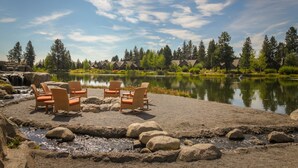 A lakeside seating area with chairs and a table, surrounded by rocks and trees. - 6 Bdrm - Caldera Springs: Lodge on the Pond (Bend)
