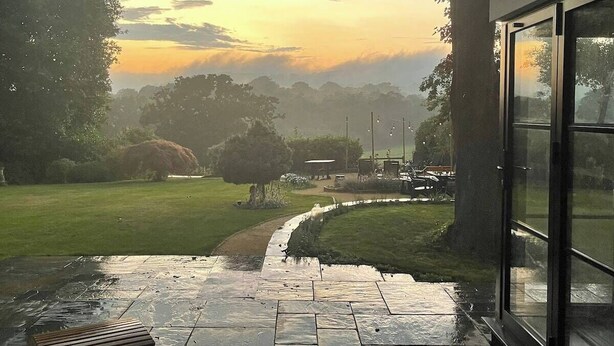 Un patio con vistas a un paisaje cubierto de césped y árboles, que da acceso a la entrada de un edificio.