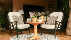Una sala de estar con dos sillones blanco y negro, una mesa redonda de madera y una alfombra estampada.