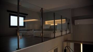 Un dormitorio moderno con un espejo grande, una cama con ropa blanca y un ventanal que proporciona luz natural.
