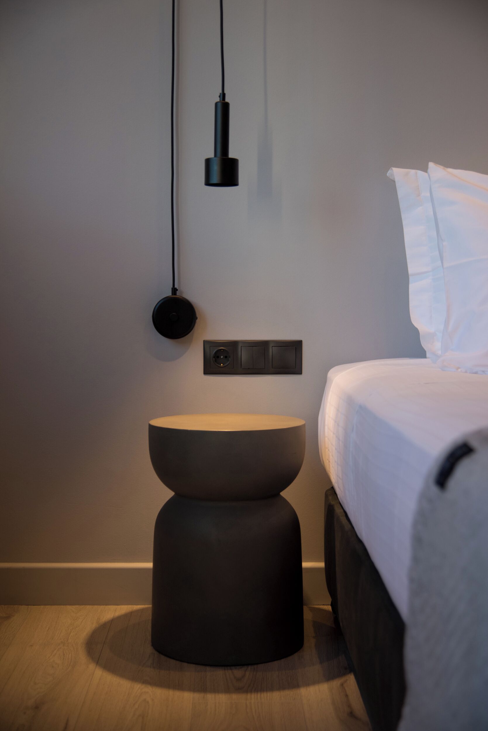 Quarto moderno com cama, mesa de cabeceira redonda, luminária fixada na parede e tomada.