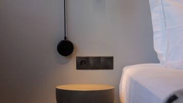Quarto moderno com cama, mesa de cabeceira redonda, luminária fixada na parede e tomada.