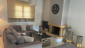 A living room with a sofa, coffee table, and ottoman, a fireplace, a television, and decorative lanterns. - ILION Air Host - Near Athens International Airport (Markopoulo Mesogaias)