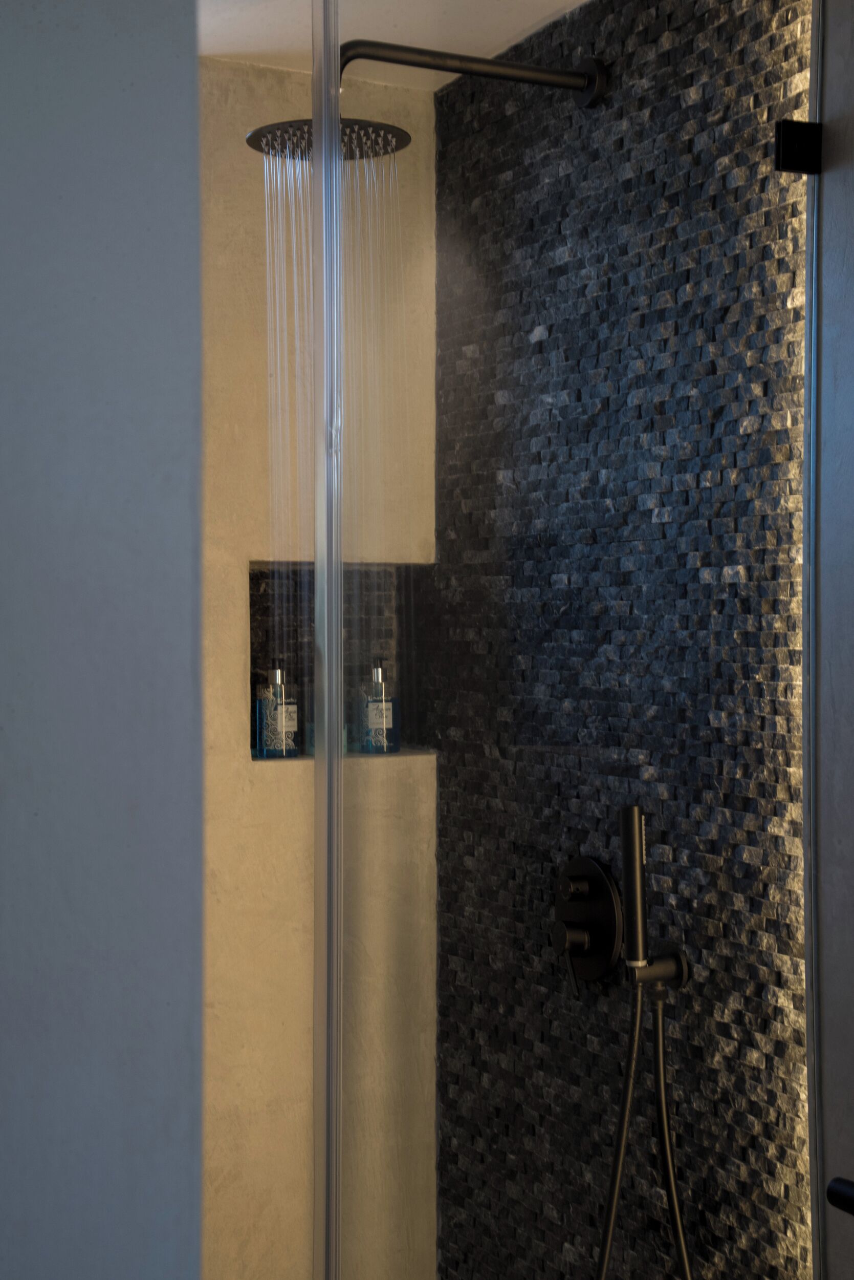 A modern shower with a glass enclosure, a stone wall, and a handheld showerhead.