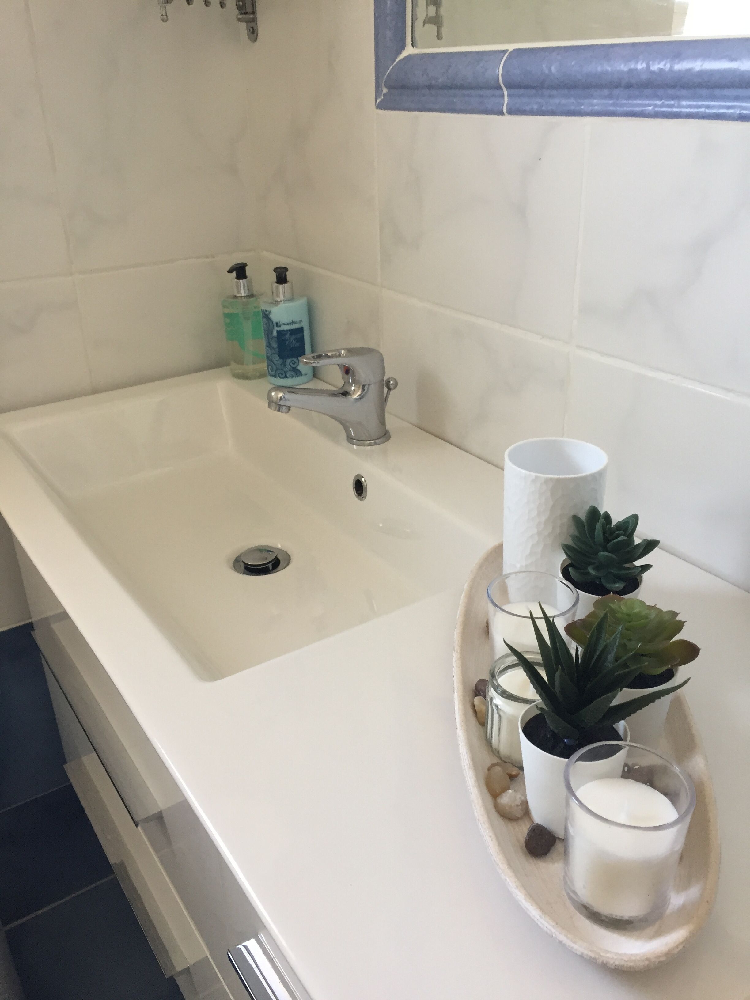 A bathroom with a white sink, a faucet, a soap dispenser, and a glass candle holder with candles and succulents.
