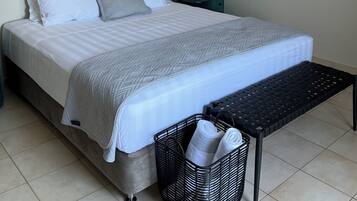 A neatly made bed with a grey and white duvet, a black bedside lamp, and a black woven bench.