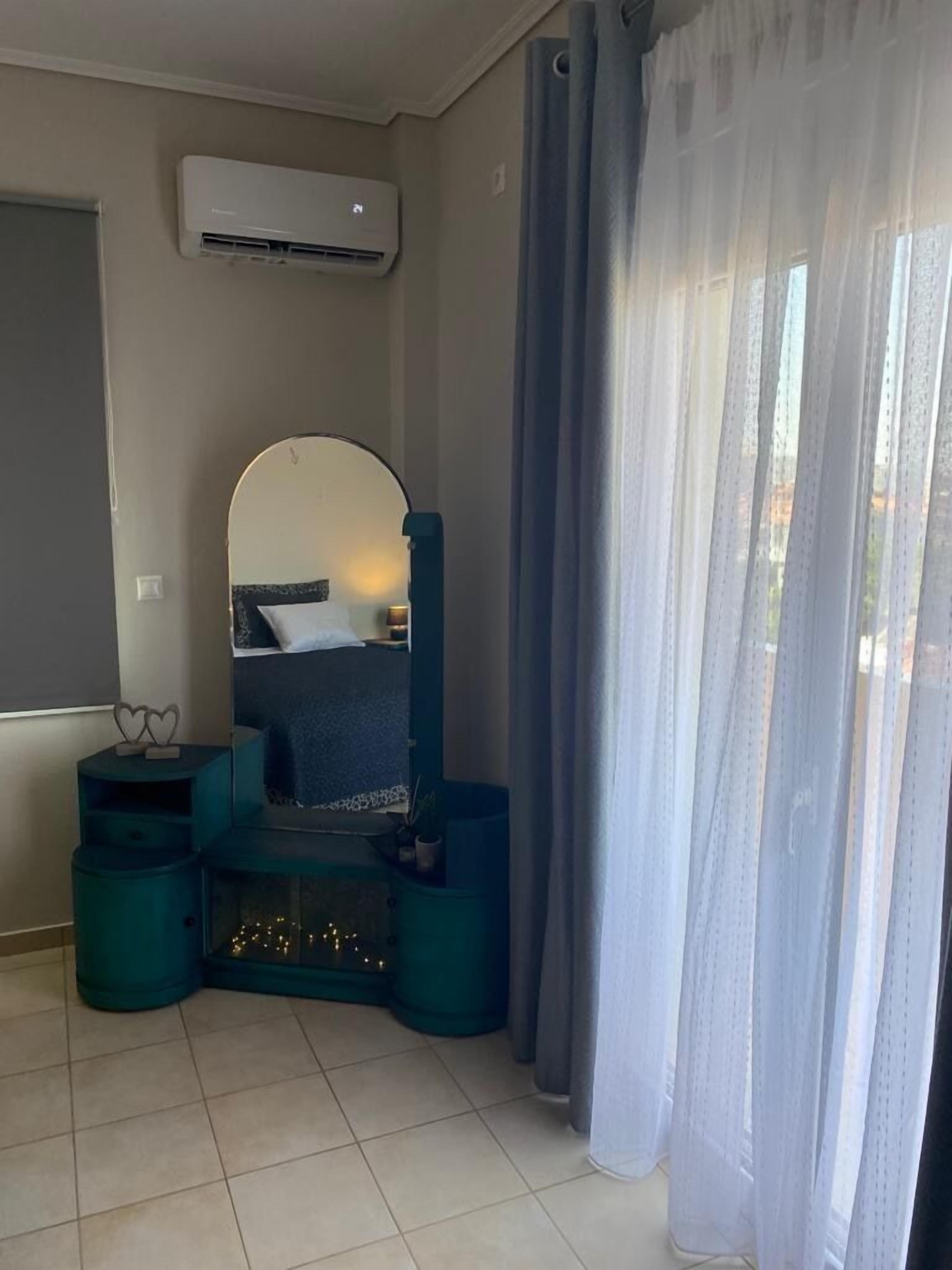 Una habitación con cama, espejo, una mesita y ventana con cortinas.