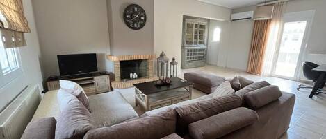 A living room with a sofa set, a television, a fireplace, and a clock on the wall.