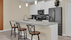 A modern kitchen with a central island, bar stools, stainless steel appliances, and pendant lighting.