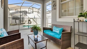 A modern living room with a glass coffee table, wicker sofa, and a view of a pool and outdoor area.