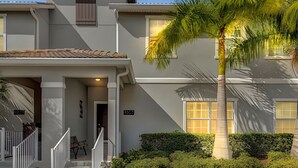 A two-story building with a covered porch, a staircase, and a palm tree.
