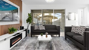 A modern living room with a black sofa, white coffee table, and a large window overlooking a cityscape. - Amazing Home Solara Resort Comfort and Leisure (Kissimmee)