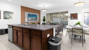A modern kitchen with a central island, built-in cabinets, and a dining area with a table and chairs. - Amazing Home Solara Resort Comfort and Leisure (Kissimmee)