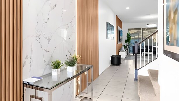 A modern hotel lobby with a marble reception desk, wooden paneling, a glass staircase, and a view of the interior. - Amazing Home Solara Resort Comfort and Leisure (Kissimmee)