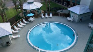 A circular pool with lounge chairs and umbrellas, surrounded by a wooden deck and a covered seating area. - Beautiful 2-bedroom condo with AC, WiFi and direct beach access in Gulf Shores (Gulf Shores)