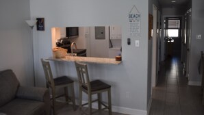 A kitchen with a bar counter, two wooden chairs, and a dining table. - Beautiful 2-bedroom condo with AC, WiFi and direct beach access in Gulf Shores (Gulf Shores)