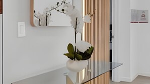 A modern interior with a glass-top table, a white orchid, and a vertical wooden panel. - Dream Home at Solara Resort 6BD and Total Comfort (Kissimmee)
