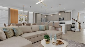 A modern living room with a beige sectional sofa, a round coffee table, and a kitchen in the background. - Dream Home at Solara Resort 6BD and Total Comfort (Kissimmee)
