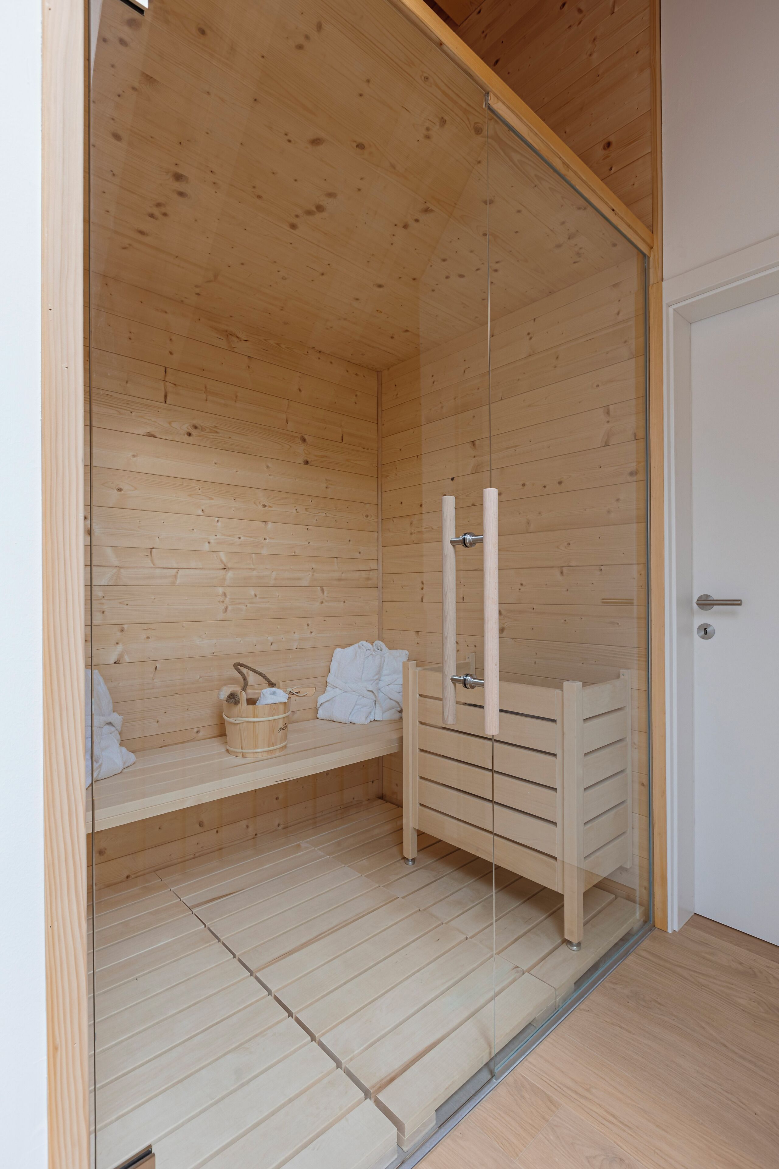 A sauna room with wooden walls and floor, a glass door, a bench, and a towel rack.