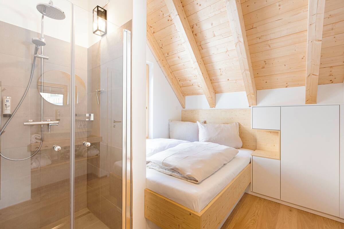 Un dormitorio moderno con ducha de vidrio, vigas de madera en el techo y almacenamiento integrado.