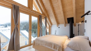 A bedroom with a large window, wooden ceiling beams, a bed, and a fireplace. - Rehfugium Lachtal by ALPS RESORTS (Oberwölz)