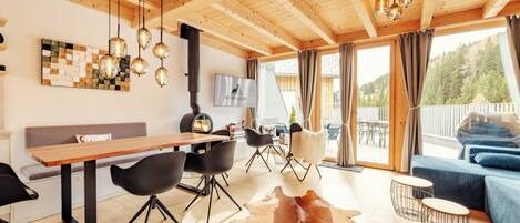 A modern interior with a wooden ceiling, a dining area with a long table and chairs, a sofa, and a cowhide rug.