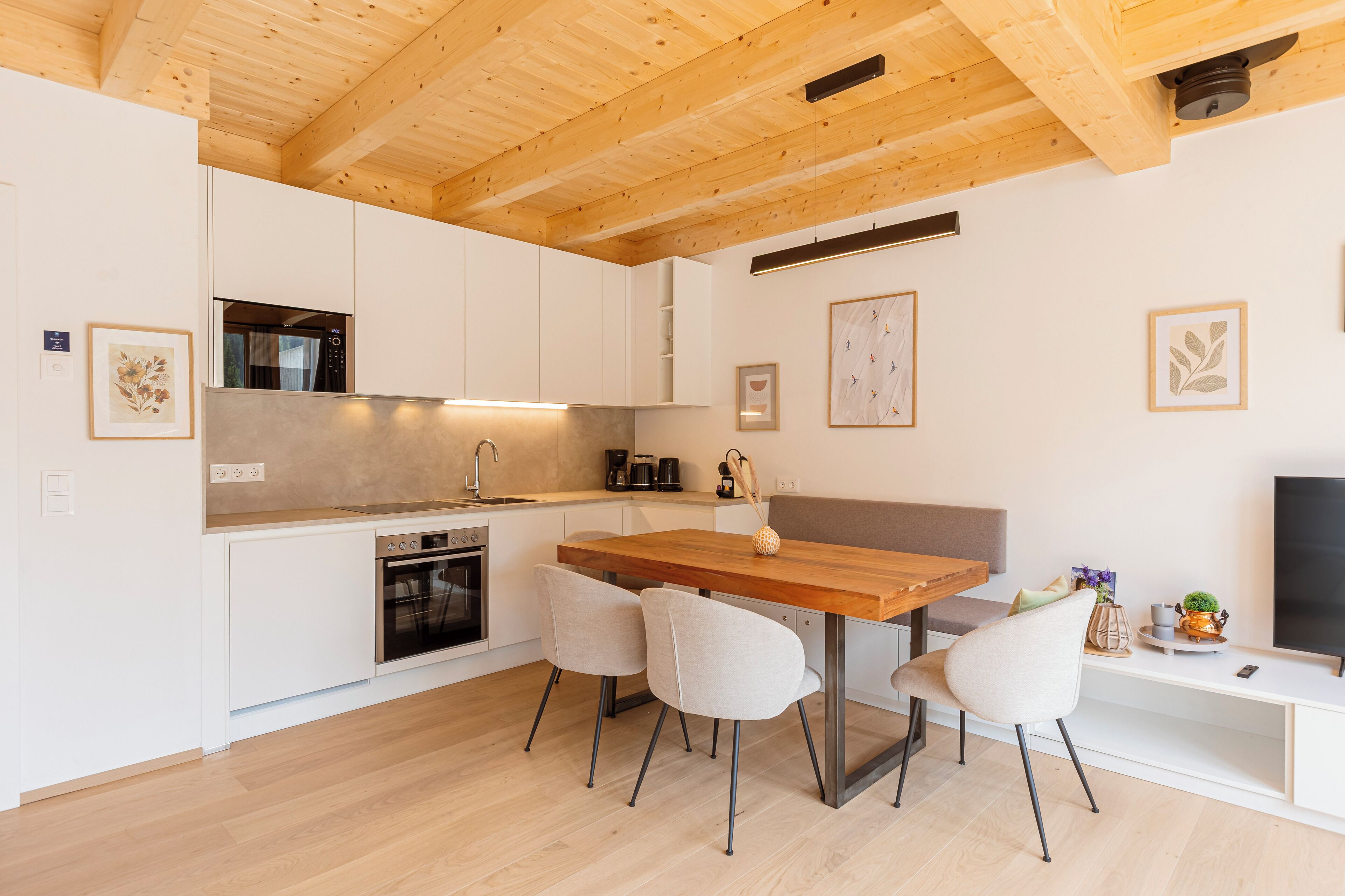 Une cuisine moderne avec des meubles blancs, une table à manger en bois et un four encastré.