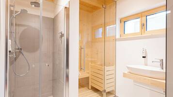 A modern bathroom with a glass-enclosed shower, wooden cabinets, and a large sink.
