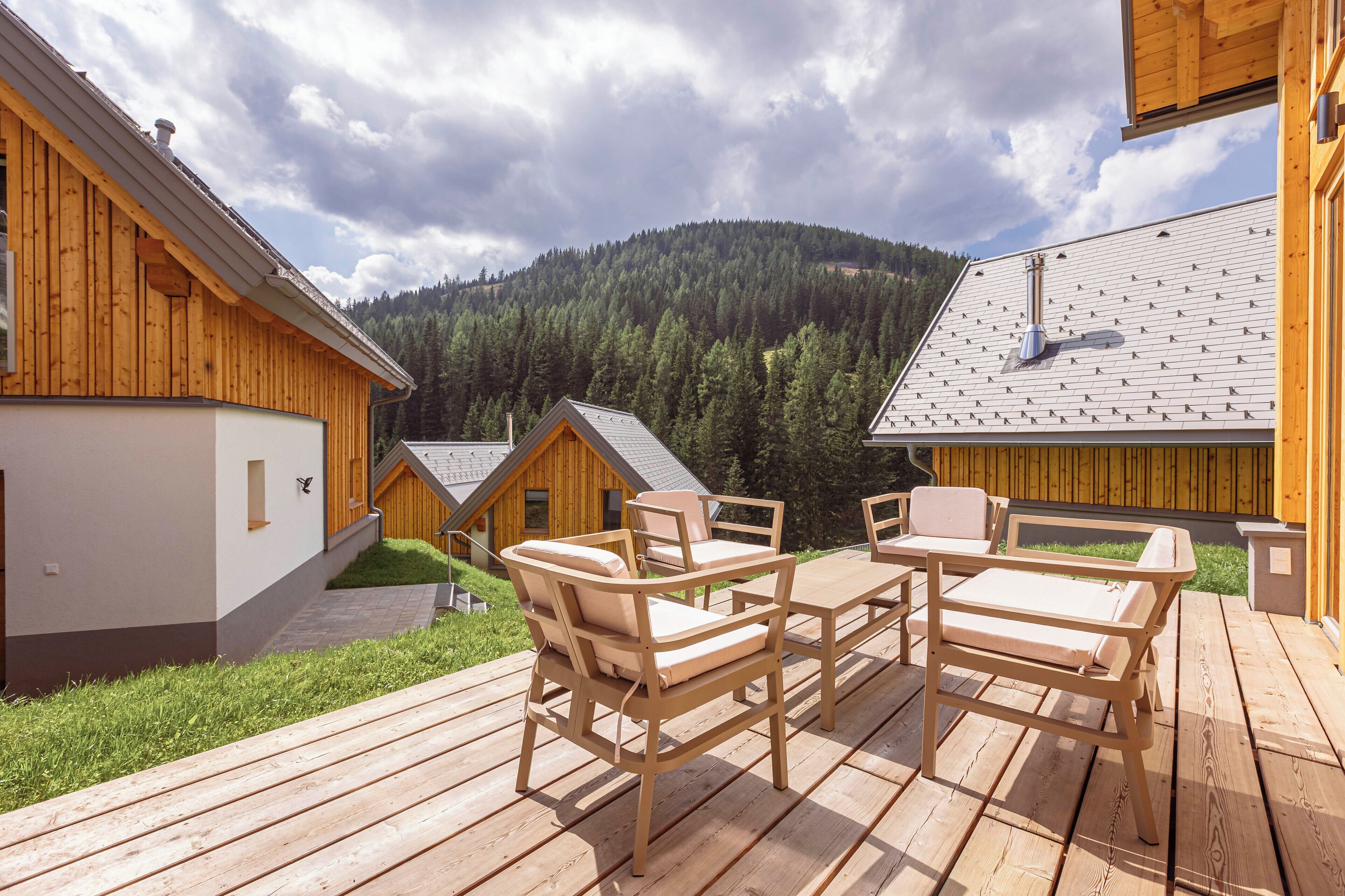A wooden deck with outdoor furniture, a mountain backdrop, and a cabin-style building.