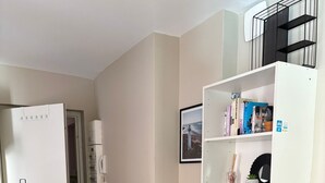 Un espacio habitable compacto con kitchenette, una pequeña zona de estar y una estantería fijada a la pared.