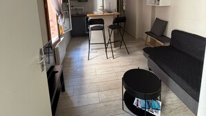 Un espacio habitable compacto con kitchenette, zona de comedor y salón con sofá y mesa de centro.