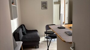 Un espacio habitable compacto con sofá, una mesita y una silla. Una puerta da a otra habitación.
