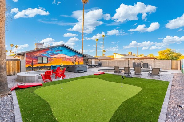 A backyard with artificial grass, a mural, outdoor furniture, and a pool.