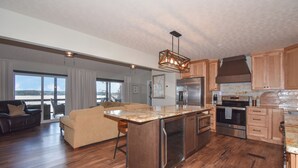 Une cuisine spacieuse avec des meubles en bois, un grand îlot central, des appareils électroménagers en acier inoxydable et une vue sur l’extérieur.
