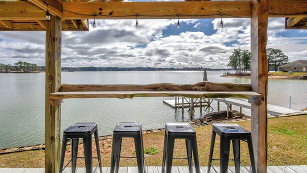 Une terrasse en bois offrant une vue sur un lac, trois tabourets et un quai.