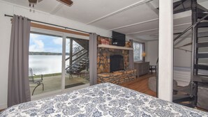 Une chambre dotée d’un grand lit, d’une cheminée en pierre et offrant une vue sur un lac grâce à une porte-fenêtre coulissante.