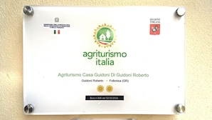Une plaque fixée au mur porte l’inscription « Agriturismo Italia » et « Agriturismo Casa Guidoni Di Guidoni Roberto », ainsi qu’un logo et le drapeau de la région de Toscane.