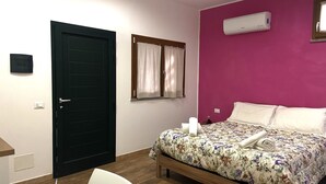 Une chambre à coucher comprenant un lit, un bureau, une chaise, une porte, un climatiseur et une fenêtre avec des rideaux.