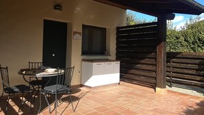 Un espace patio avec une table ronde et des chaises, un meuble blanc, une porte noire et un escalier en bois.