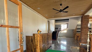 A spacious room with a wooden ceiling, a reception desk, a staircase, and a view of the outdoors.