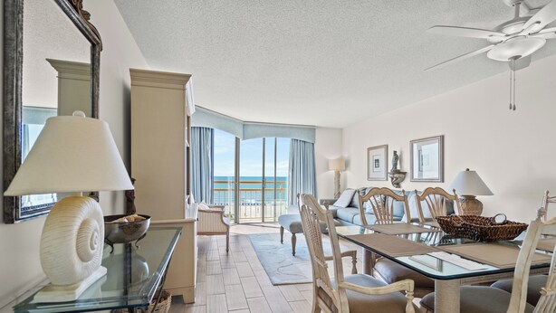 A spacious dining area with a glass table, wooden chairs, and a view of the ocean. - Oceanfront 3-bedroom Condo - North Myrtle Beach (Myrtle Beach)