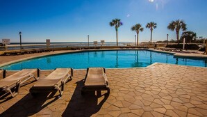 A pool with lounge chairs and palm trees, a clear sky, and a lifeguard sign. - Oceanfront 3-bedroom Condo - North Myrtle Beach (Myrtle Beach)