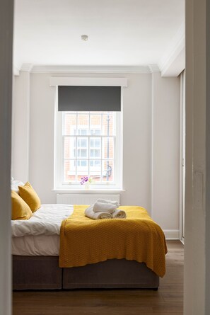 A bedroom with a bed, a window with a view of buildings, and a radiator. - 4-bdr Stunning Kensington Penthouse (London)