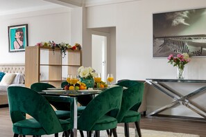 A dining area with a table set for six, surrounded by green velvet chairs. A wooden cabinet with a floral arrangement is in the background, and a framed picture is on the wall. - 4-bdr Stunning Kensington Penthouse (London)