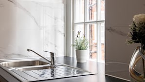 A kitchen with a stainless steel sink, a potted plant, and a window with a view of brick buildings. - 4-bdr Stunning Kensington Penthouse (London)