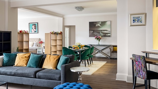 A modern living room with a grey sofa, green chairs, and a dining area with a table and chairs. - 4-bdr Stunning Kensington Penthouse (London)