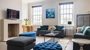 A modern living room with a fireplace, sofas, ottomans, and artwork on the walls. - 4-bdr Stunning Kensington Penthouse (London)