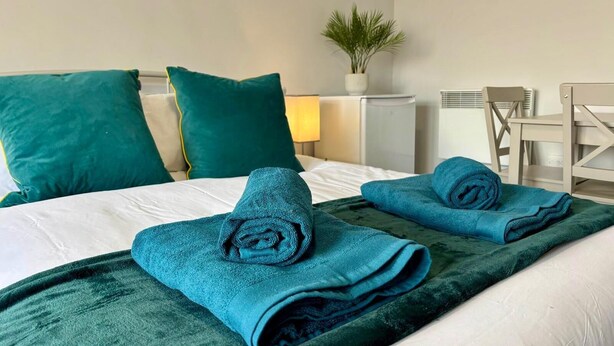 Una camera d'albergo con un letto, due cuscini color acquamarina, una coperta color acquamarina e una piccola pianta in vaso.