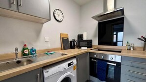 Una cucina compatta con lavatrice, forno a microonde, fornello e lavandino.