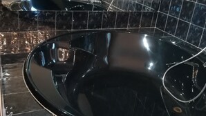 Ein modernes Badezimmer mit einer schwarzen Badewanne, glänzenden schwarzen Fliesen und einem sichtbaren Waschbereich.